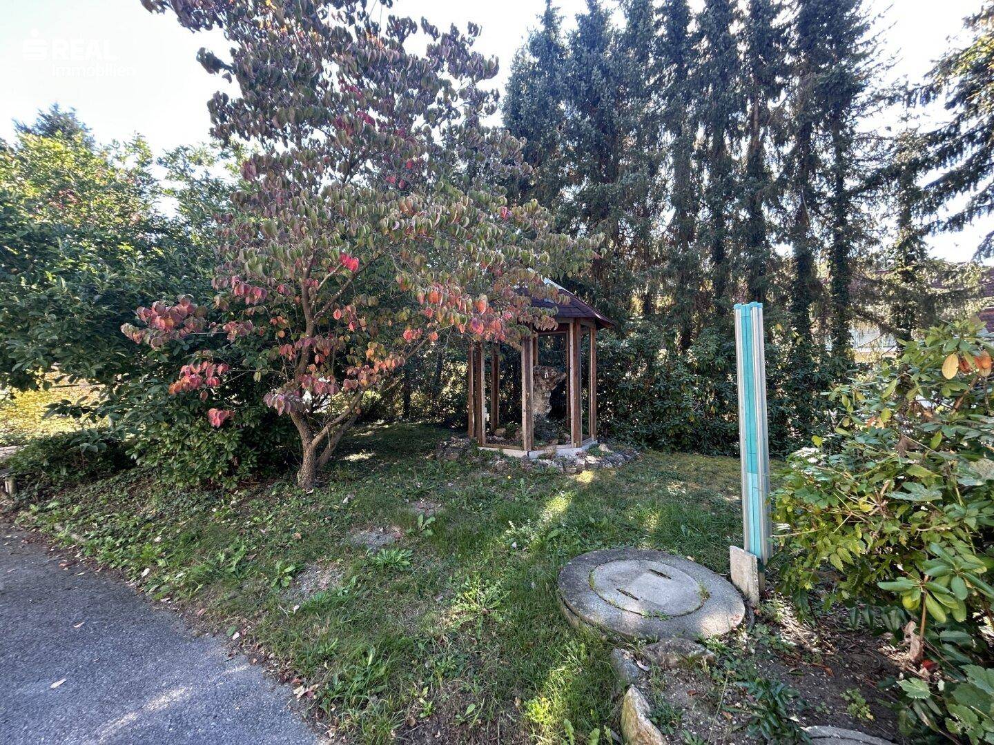 Gartenbereich mit Rasenfläche, Bäumen und einem kleinen Holzpavillon.