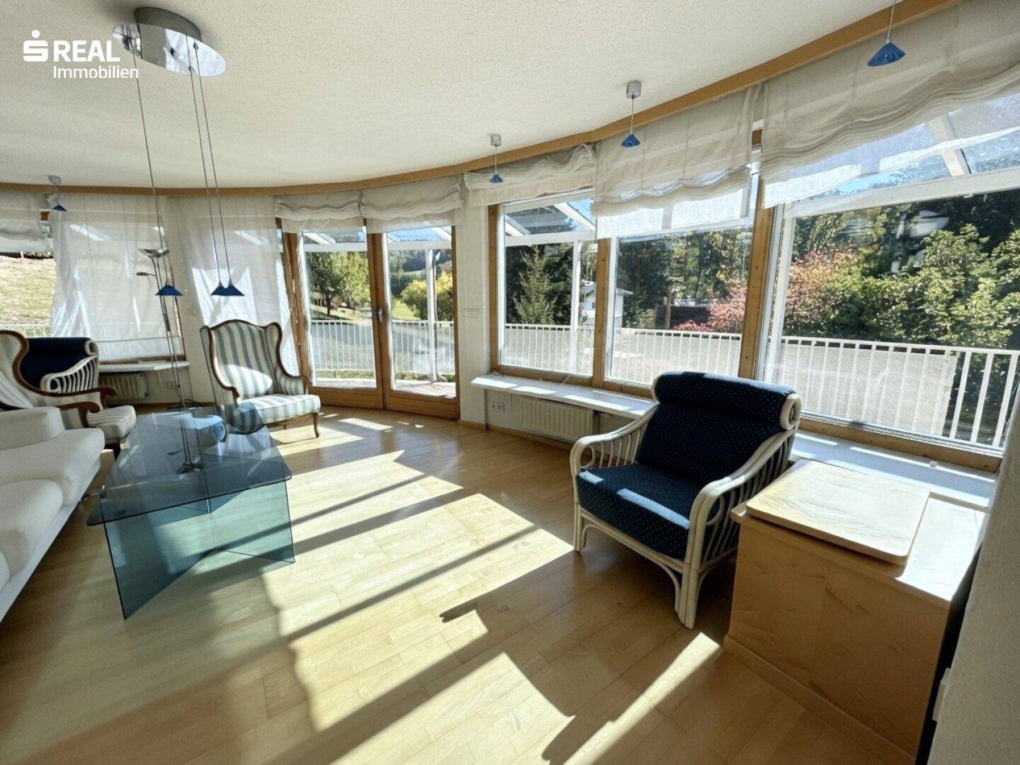 Lichtdurchflutetes Wohnzimmer mit großen Panoramafenstern und Zugang zum Balkon.