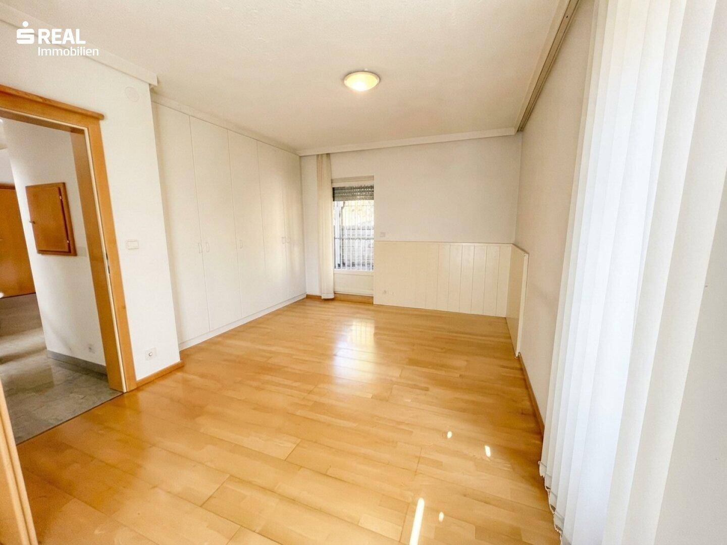 Geräumiges Schlafzimmer mit Holzboden, Einbauschränken und Fenster.
