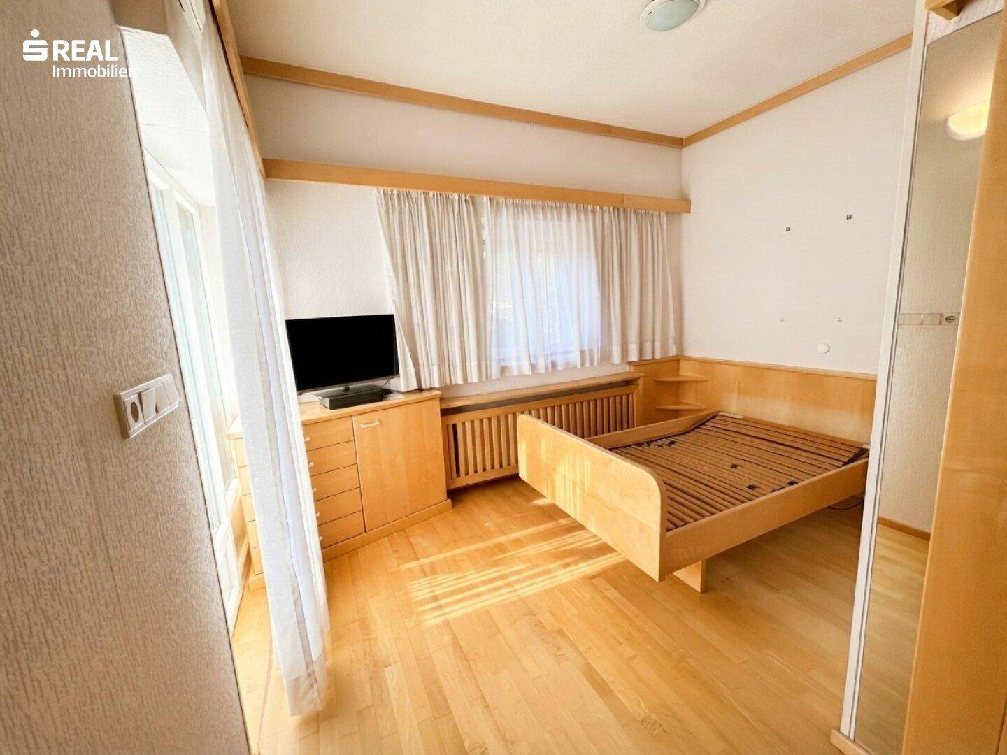 Helles Schlafzimmer mit Holzboden, Einzelbett und Fenster mit Vorhängen.