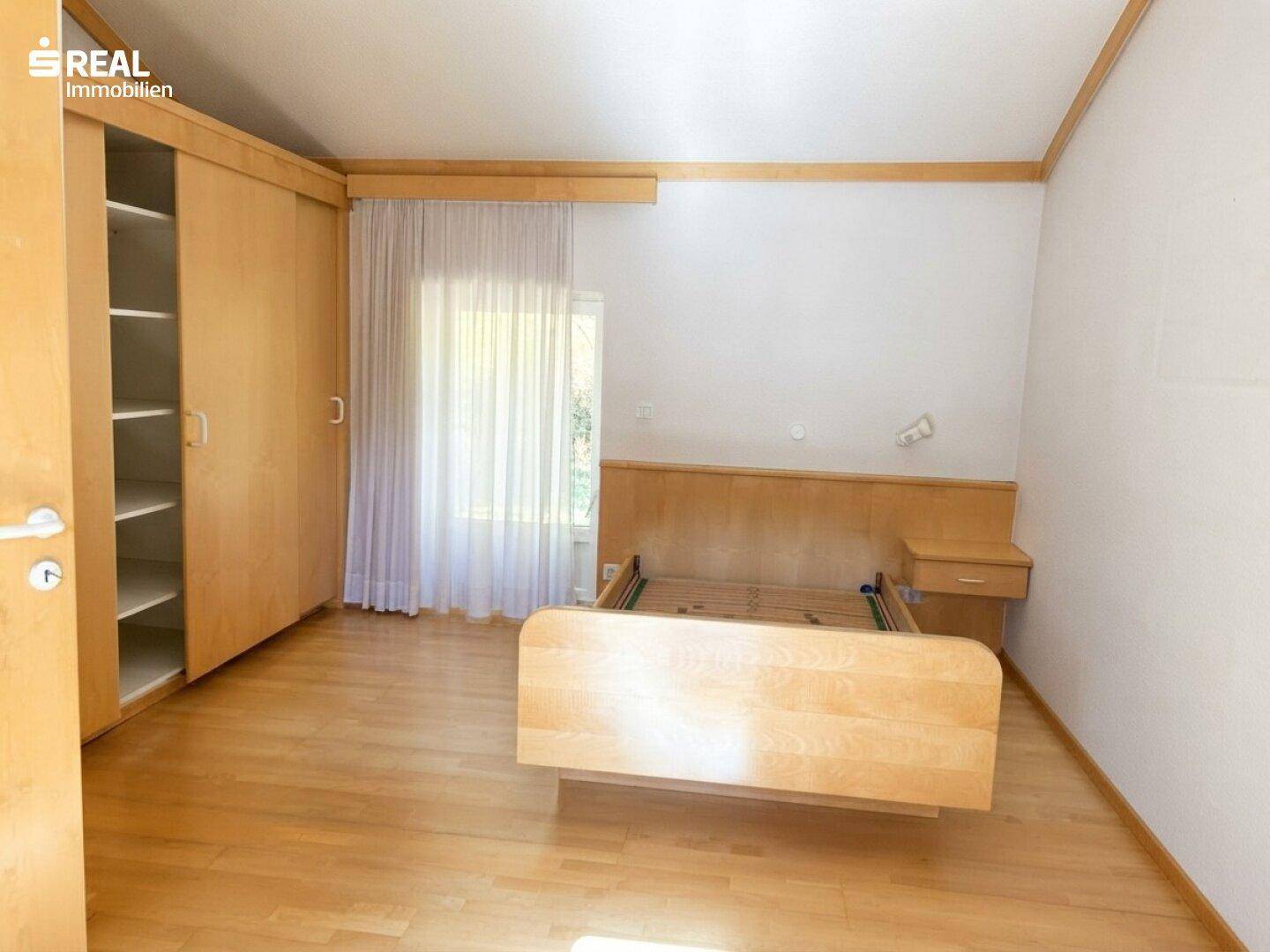 Schlafzimmer mit Holzboden, Bettgestell und großem Einbauschrank.