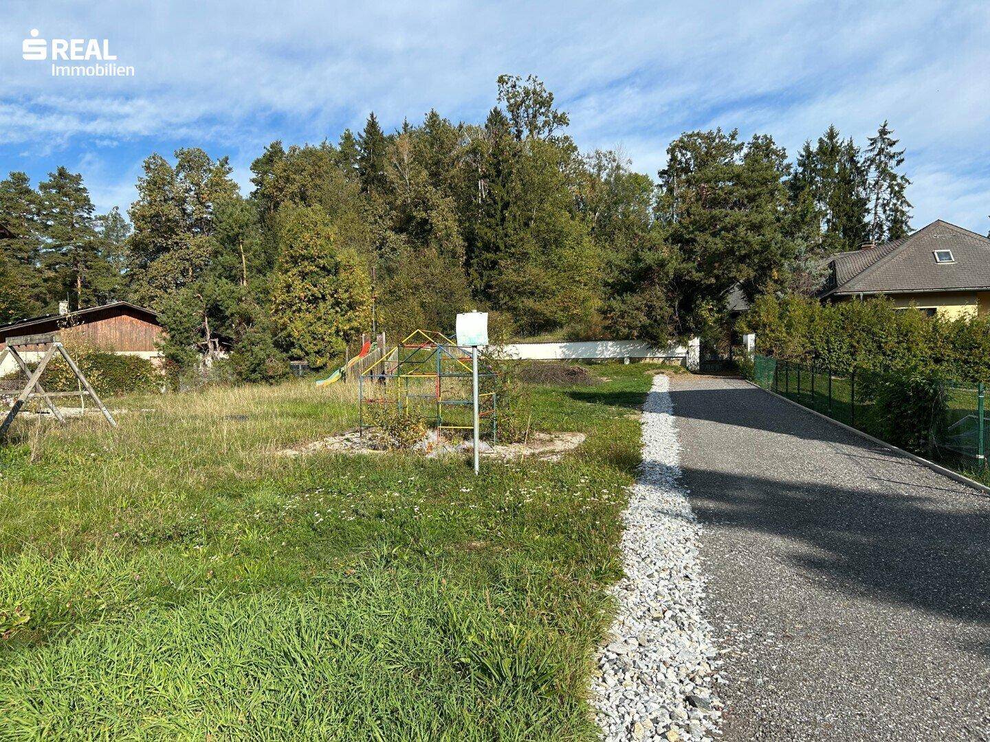 Weitläufiges Gartengrundstück mit Schotterweg und angrenzenden Häusern.