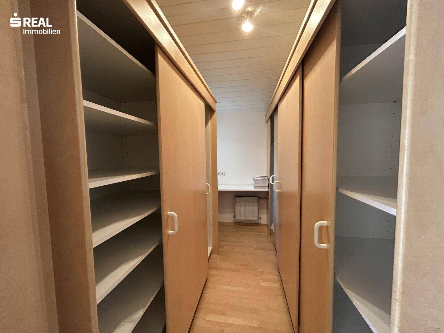 Praktischer begehbarer Kleiderschrank mit vielen Regalen und Holzschiebetüren.