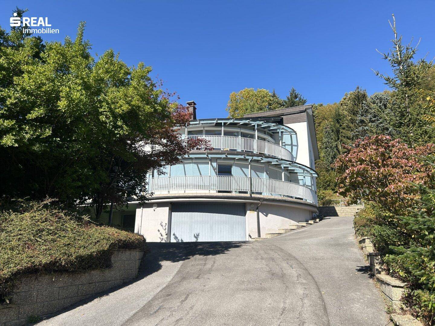 Großzügiges Wohnhaus mit weitläufiger Auffahrt und umgebender Natur unter klarem Himmel.