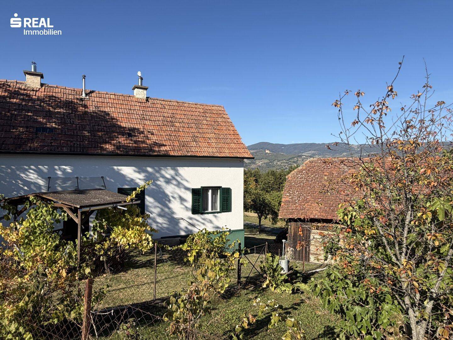 Ländliches Anwesen mit traditionellem Haus und kleinem Weinberg im Vordergrund, umgeben von Hügeln.