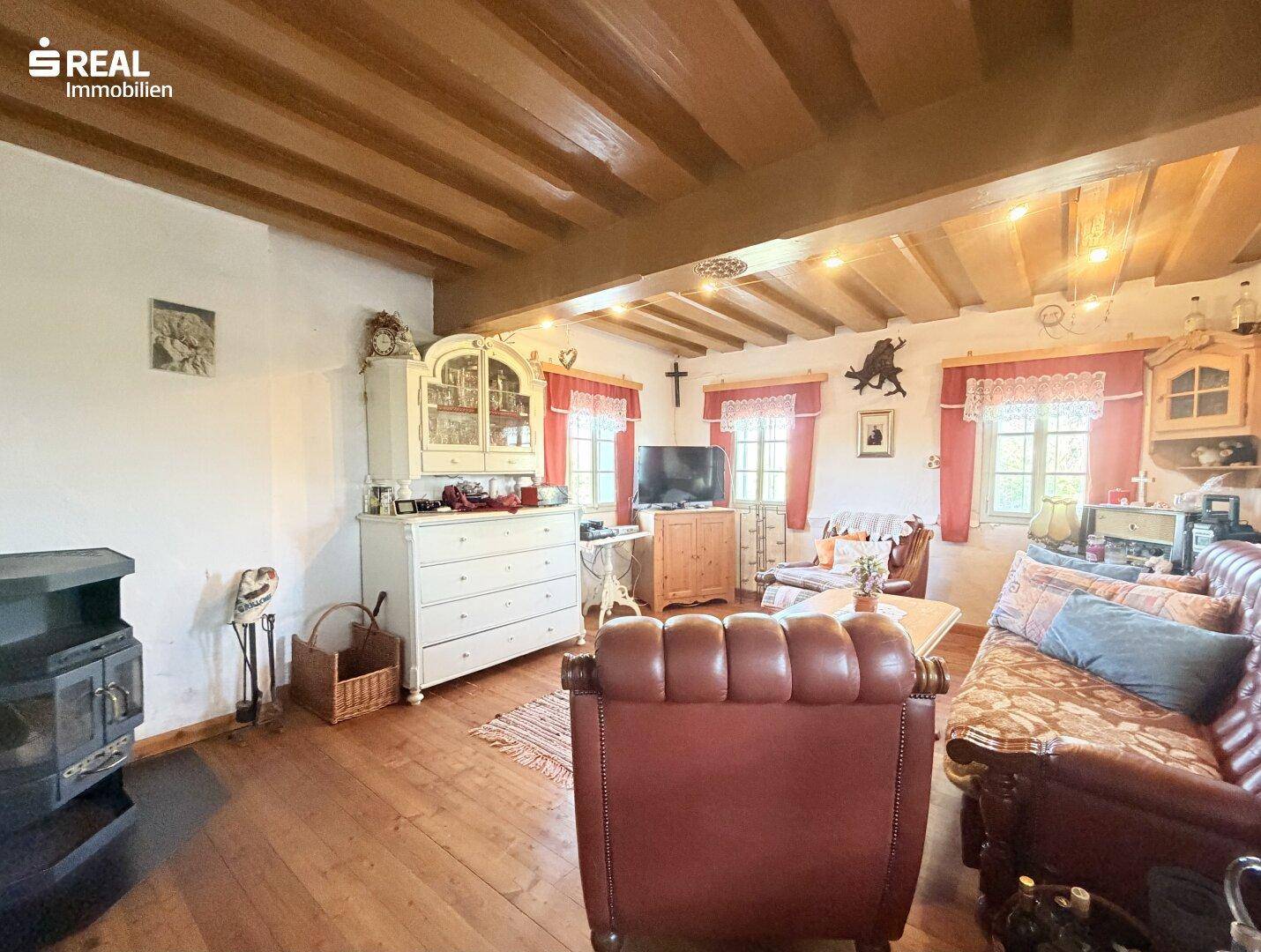 Rustikales Wohnzimmer mit Holzbalkendecke, Kaminofen und traditionellen Möbeln, strahlt Gemütlichkeit aus.
