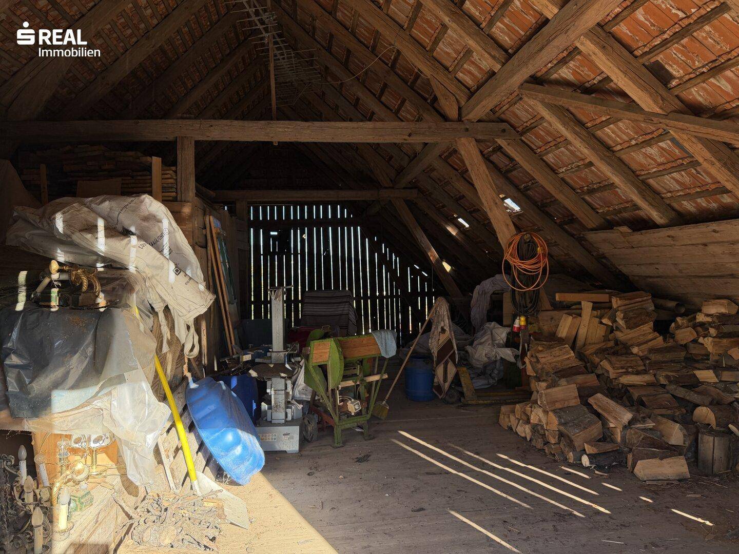 Geräumiger Dachboden mit Holzbalken und gelagertem Brennholz, bietet viel Stauraum.