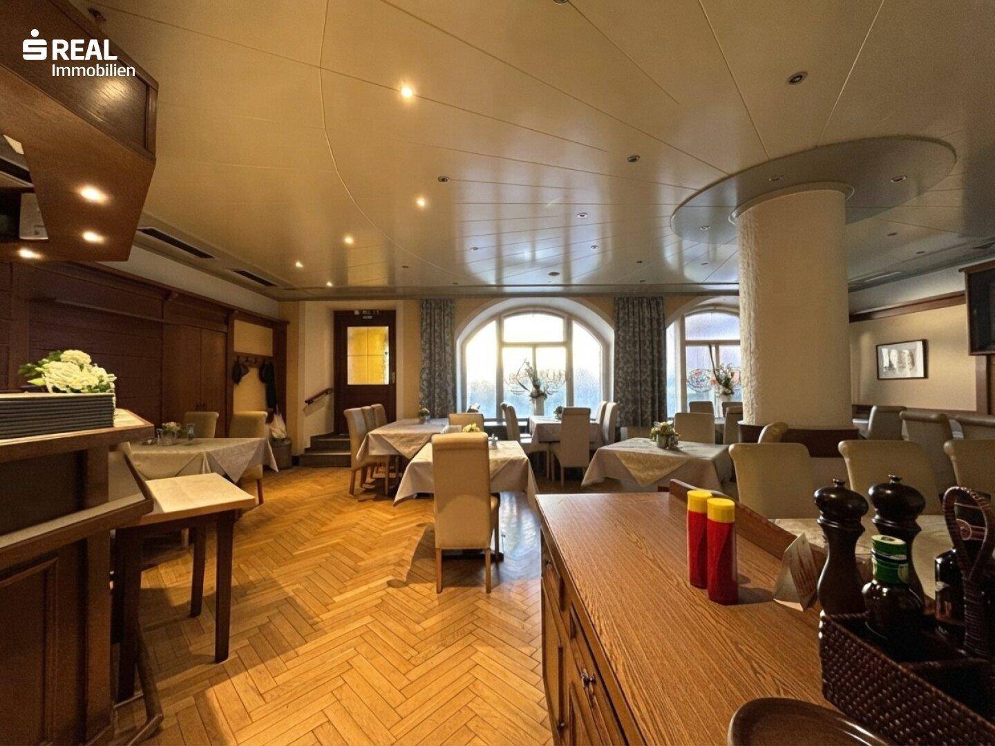 Geräumiger Speisesaal mit Holzboden, runden Fenstern und festlich gedeckten Tischen, bereit für Gäste.