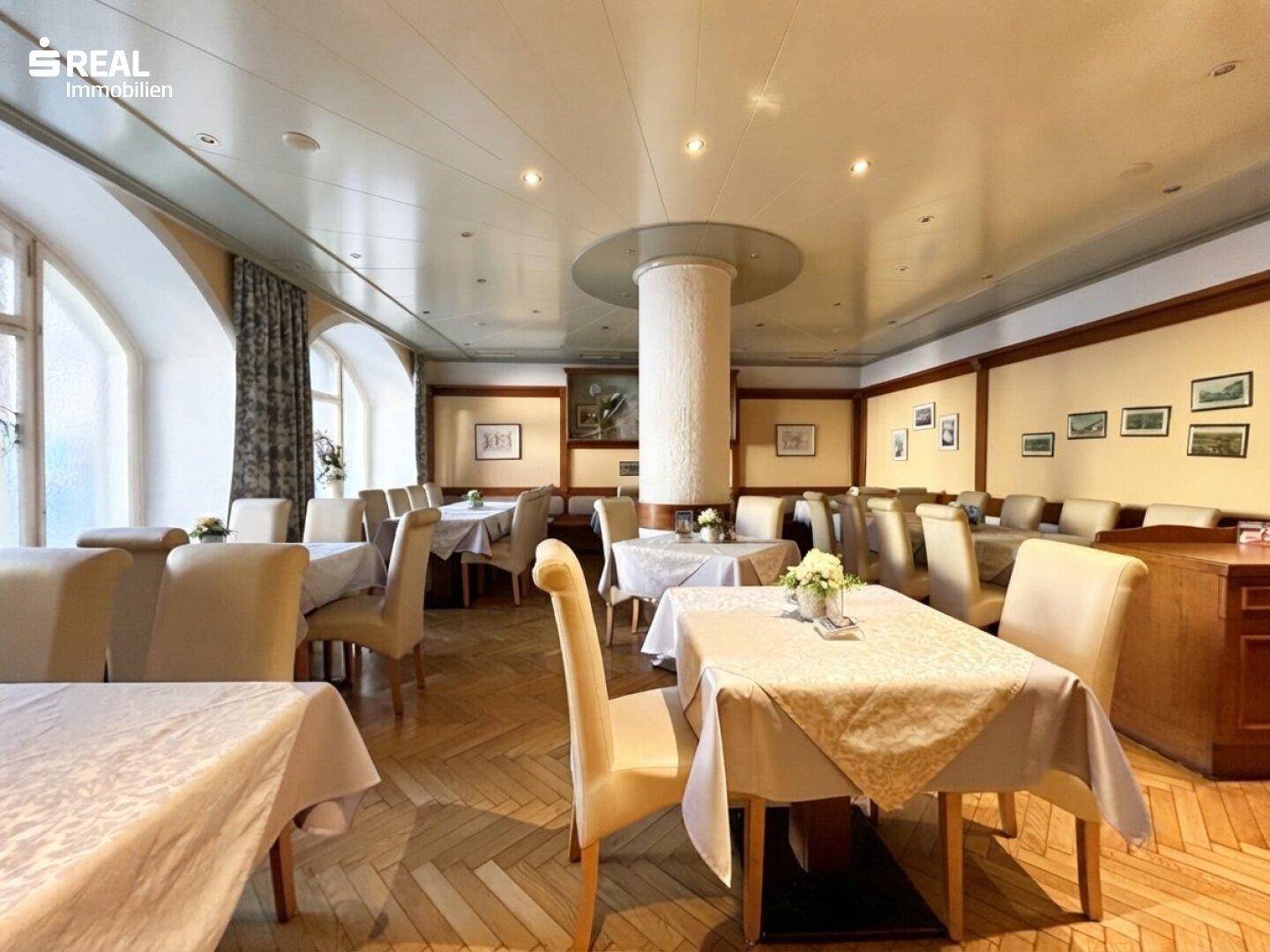 Heller Speisesaal mit elegant gedeckten Tischen, Parkettboden und großen Fenstern, die viel Tageslicht hereinlassen.
