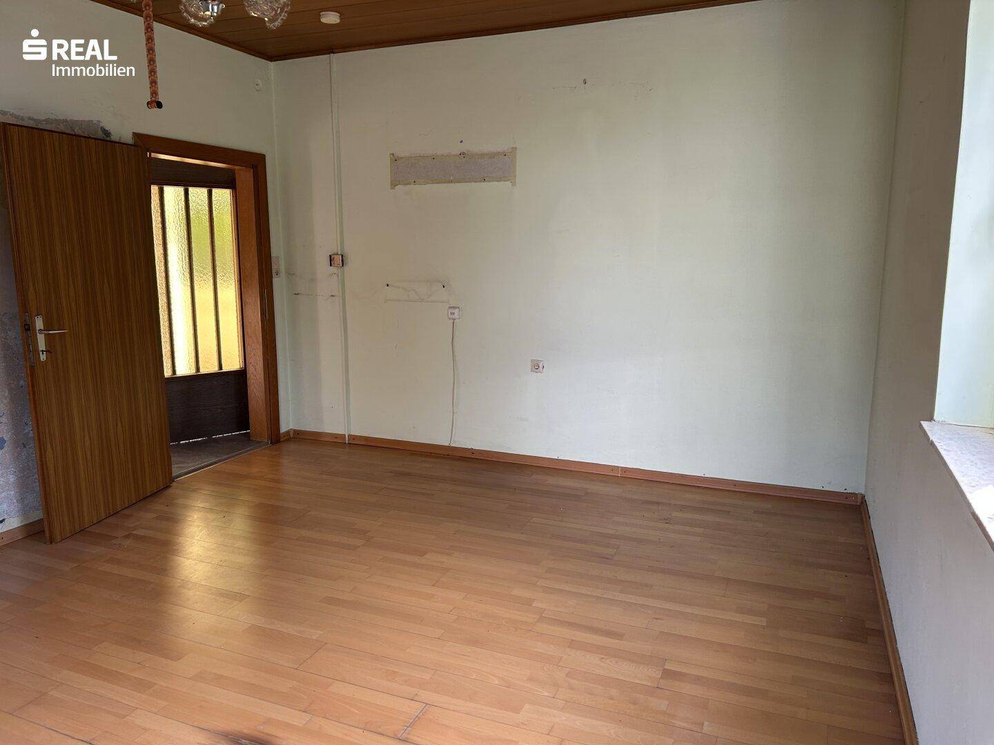 Geräumiger Wohnraum mit Parkettboden, Holzdecke und Zugang zu einem weiteren Bereich.