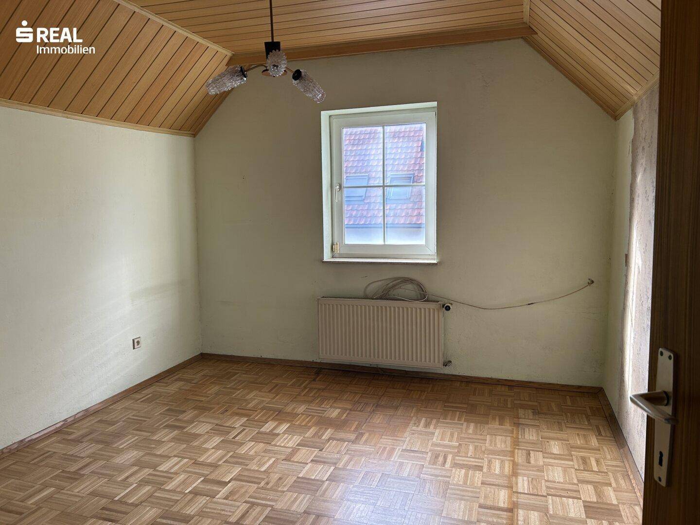 Schlafzimmer im Dachgeschoss mit Holzdecke, Parkettboden und Fenster in der Dachschräge.