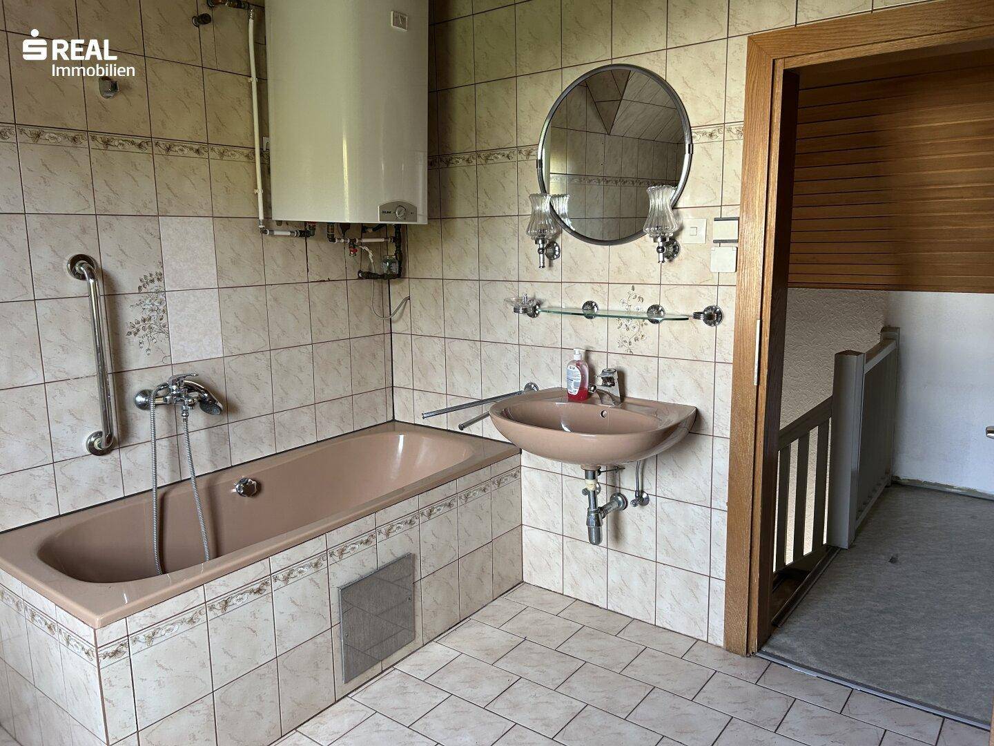 Badezimmer mit Badewanne, Waschbecken, Spiegel und Warmwasserboiler an der Wand.
