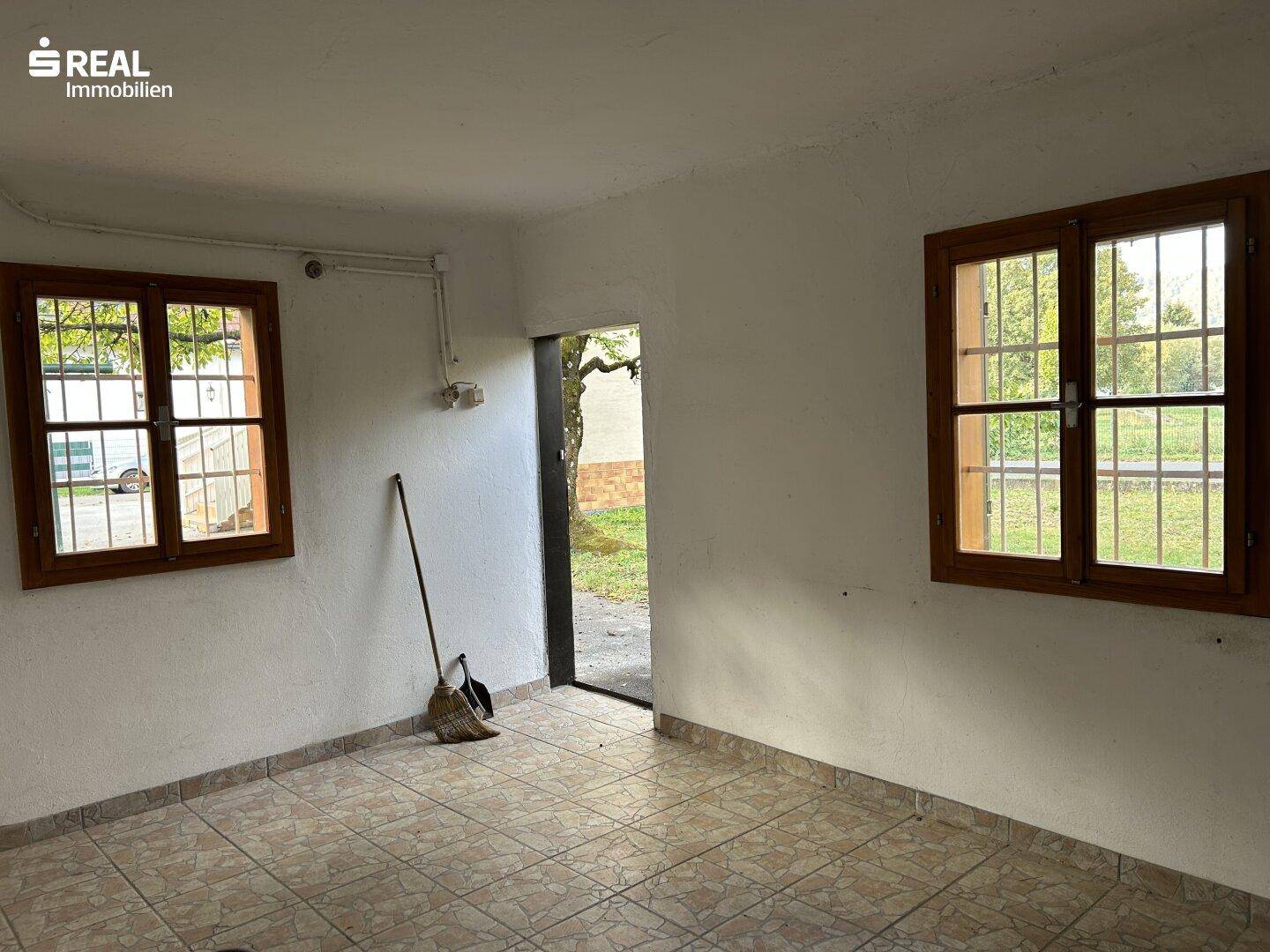 Innenraum des Nebengebäudes mit Fliesenboden, Fenstern und Zugang zum Garten.