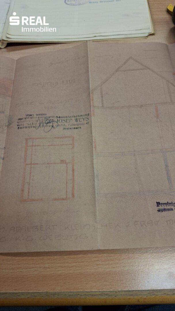Historischer Bauplan mit handschriftlichen Vermerken und roten Markierungen auf vergilbtem Papier.