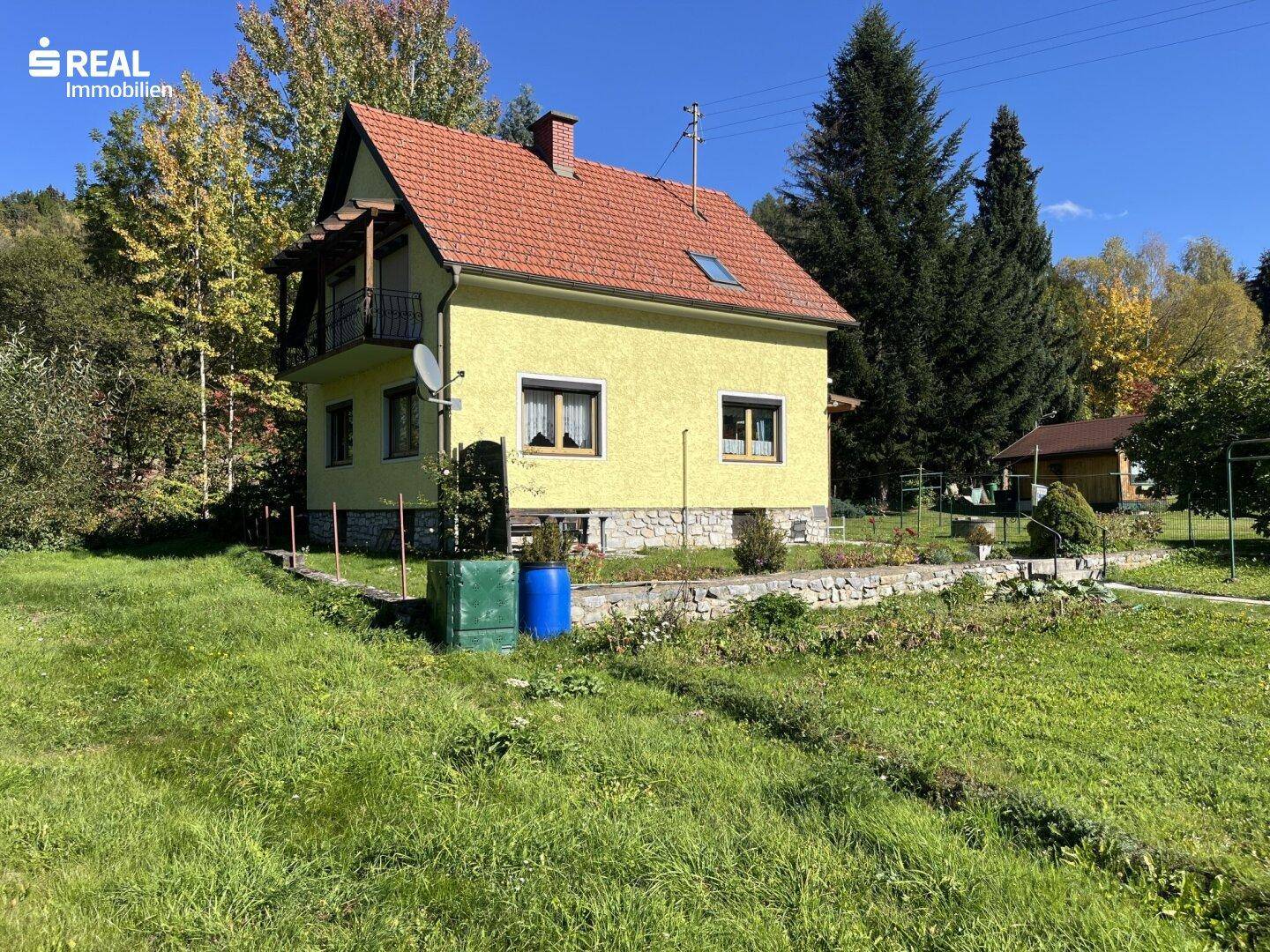 Freistehendes Haus mit gelber Fassade und rotem Dach, umgeben von viel Grün und Bäumen.