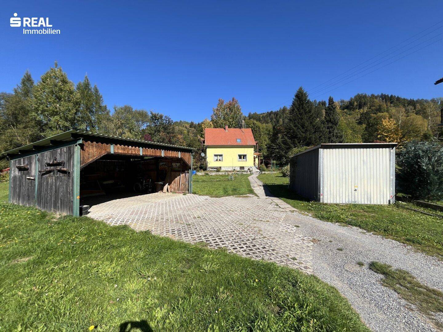 Weitläufiges Grundstück mit Einfamilienhaus im Hintergrund, Holzschuppen und Carport.