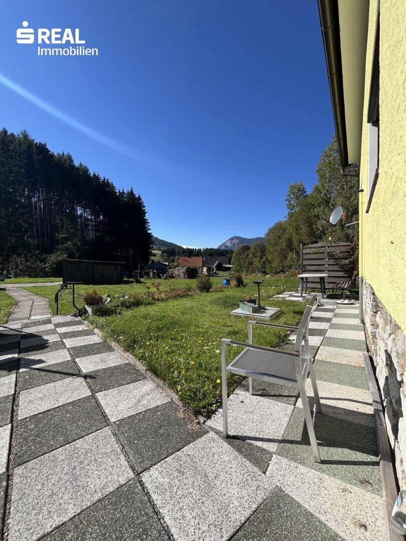 Gepflasterter Sitzbereich vor dem Haus mit Gartenmöbeln und weitem Blick auf die Landschaft.