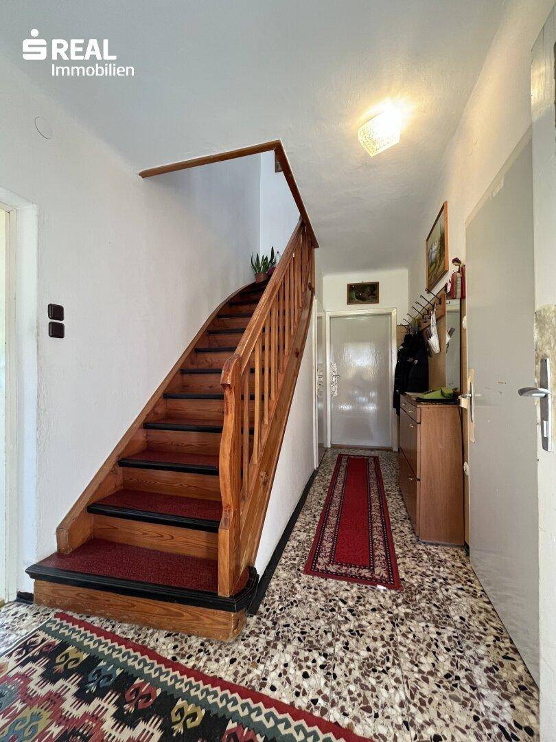 Flur mit Holztreppe und gemustertem Teppich, der in die obere Etage des Hauses führt.