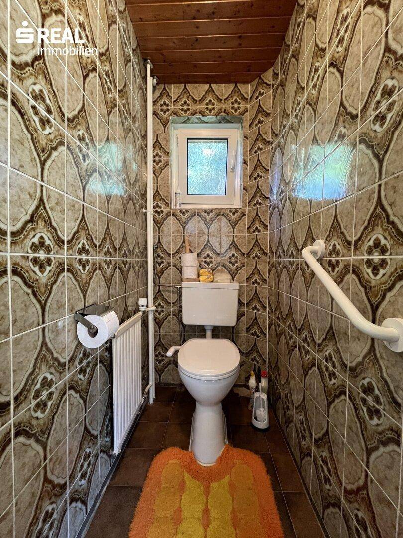 Separate Toilette mit gemusterten Fliesen, Fenster und Haltegriffen für Barrierefreiheit, sauber.