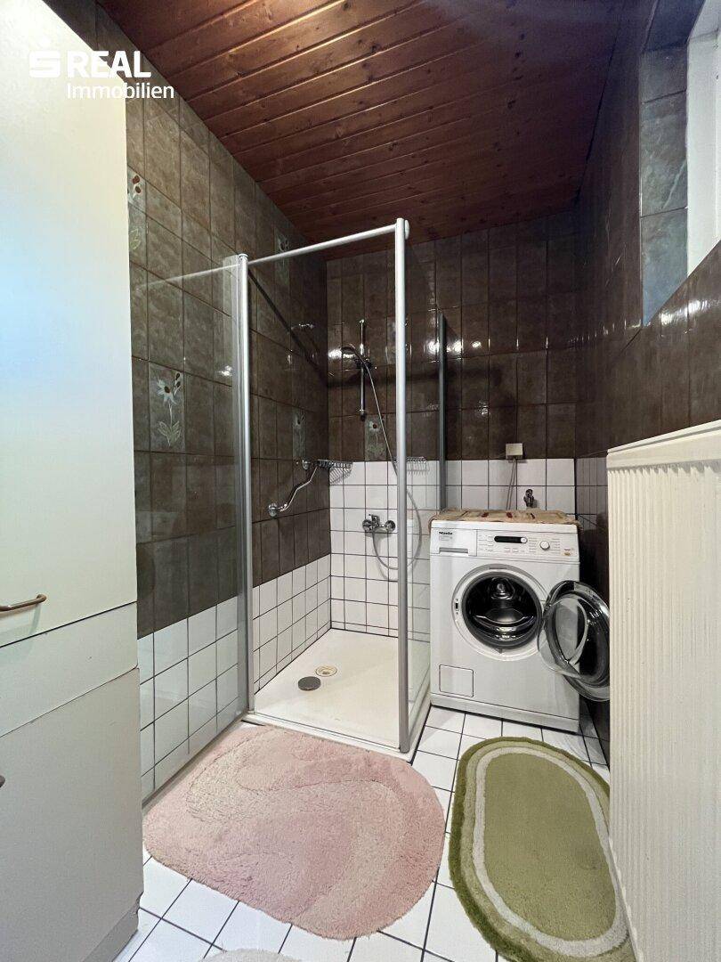 Badezimmer mit Duschkabine, Waschmaschine und braunen Fliesen an Wänden und Decke, funktional.