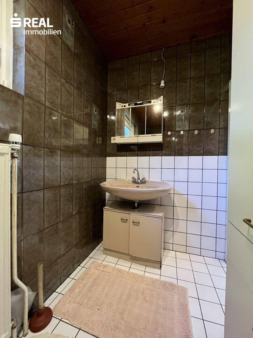 Badezimmer mit Waschbecken, Spiegelschrank und braun-weißen Fliesen im Retro-Stil, gepflegt.