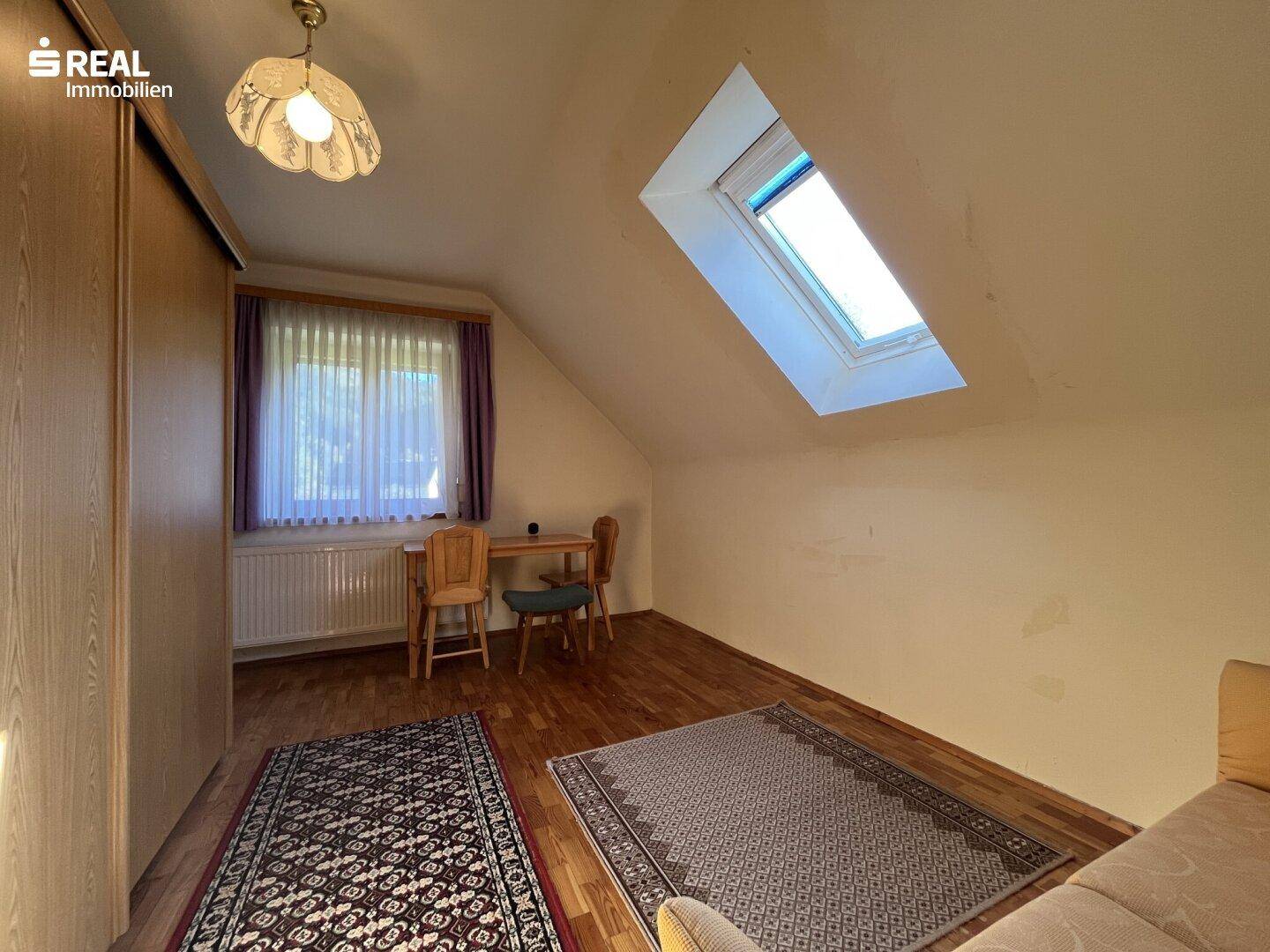 Dachzimmer mit Holzboden, Schreibtisch und großem Fenster, ideal als Schlaf- oder Arbeitszimmer.