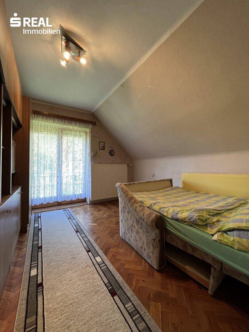 Gemütliches Schlafzimmer im Dachgeschoss mit Holzboden, schräger Decke und Fenster zum Garten.