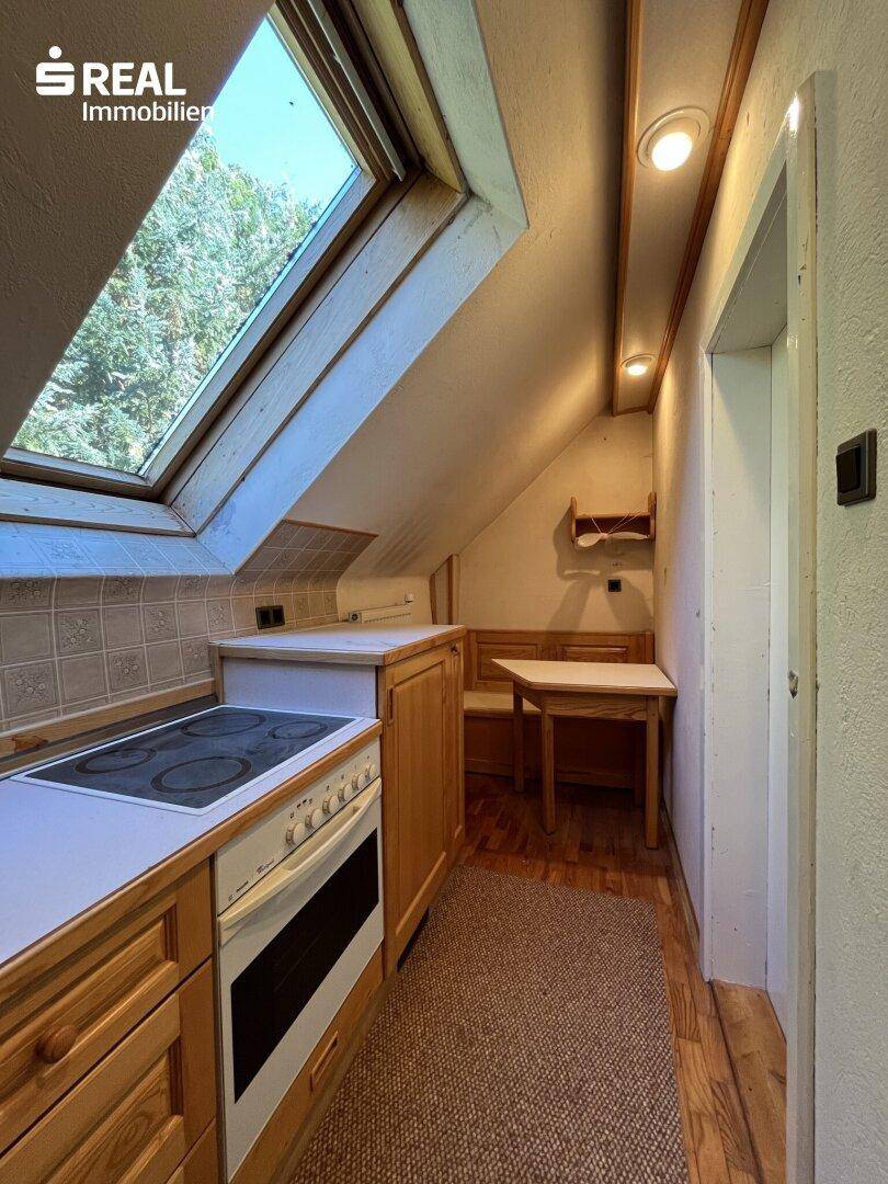 Dachgeschossküche mit Holzfronten, integriertem Essbereich und großem Dachfenster, hell und gemütlich.