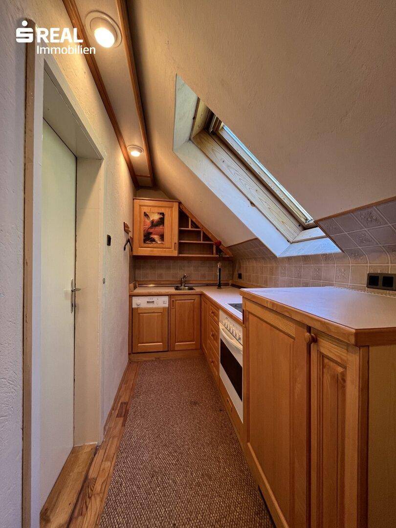 Kleine Küche im Dachgeschoss mit Holzschränken, Dachfenster und Schrägen, praktisch eingerichtet.