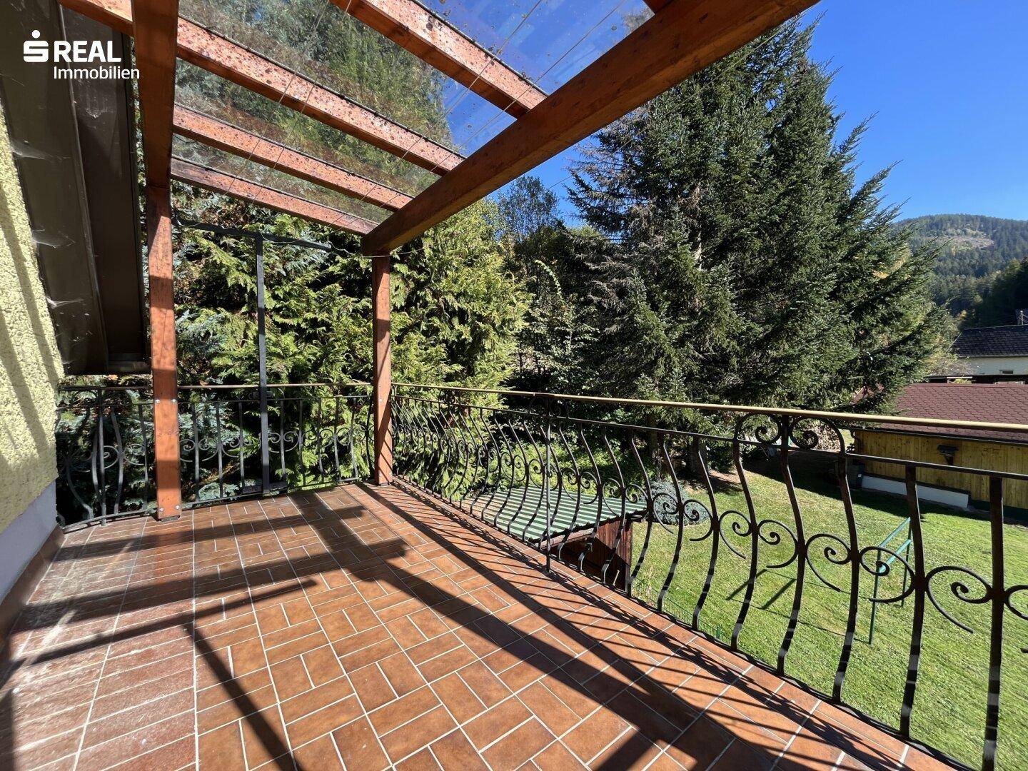Überdachter Balkon mit Blick auf dichte Bäume und die grüne, bewaldete Umgebung.