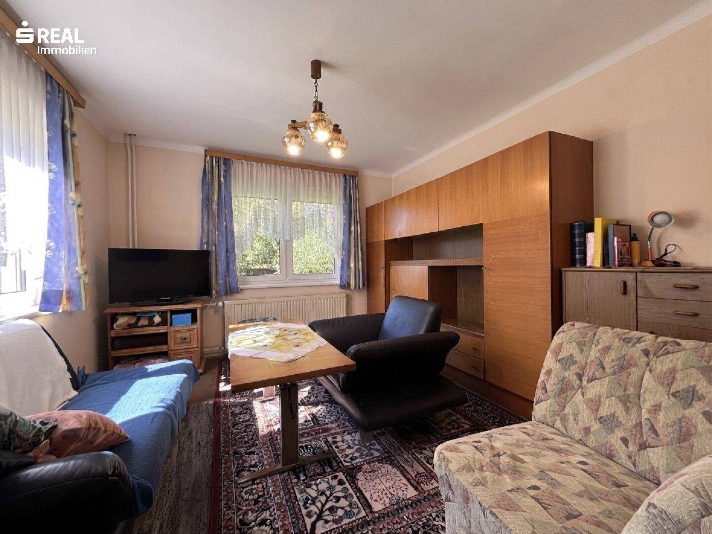 Wohnzimmer mit traditionellen Möbeln, Teppich und großem Fenster mit Vorhängen, hell und wohnlich.