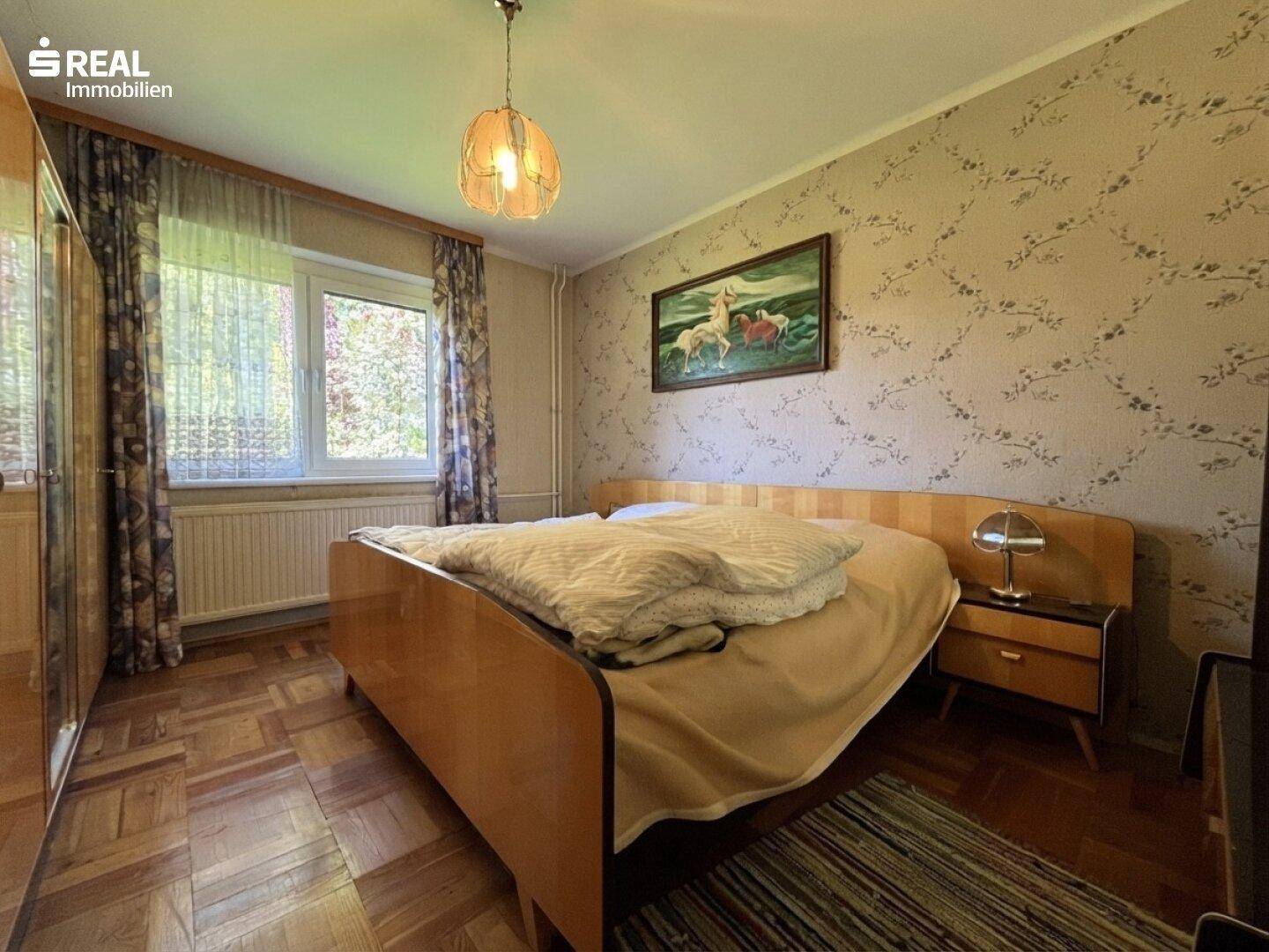 Schlafzimmer mit Doppelbett, Holzmöbeln und gemusterter Tapete, hell und gemütlich eingerichtet.