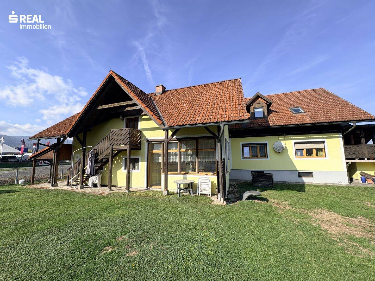 Rückansicht des Hauses mit weitläufiger Rasenfläche und einer kleinen Terrasse mit Gartenmöbeln.