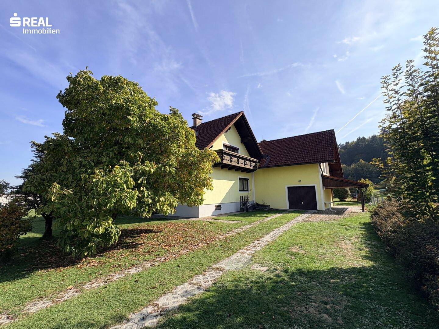 Seitenansicht des Hauses mit Garage, langer Auffahrt und altem Baumbestand im Gartenbereich.