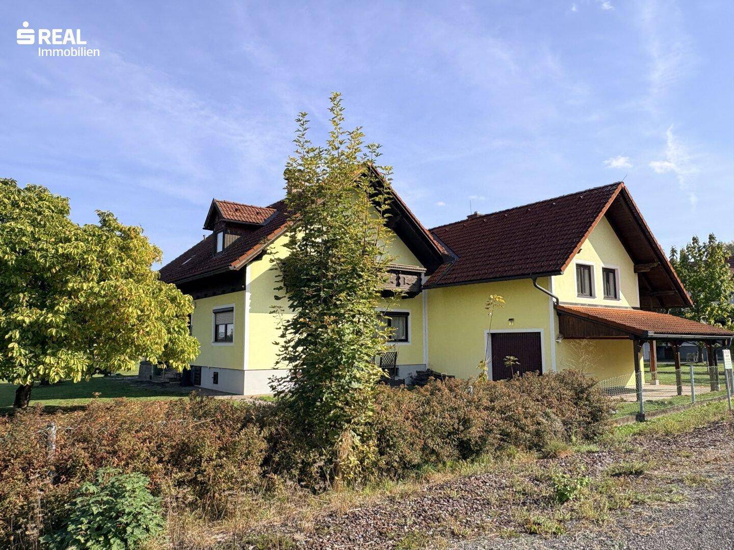 Seitenansicht des Hauses mit gepflegtem Gartenbereich und überdachtem Eingangsbereich unter blauem Himmel.