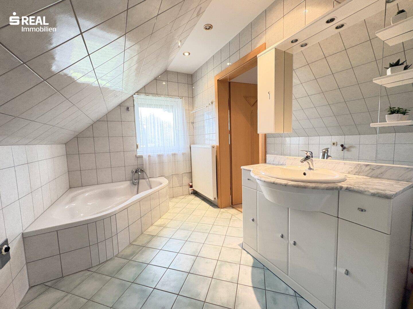 Helles Badezimmer mit Eckbadewanne, weißen Fliesen und Dachschräge.