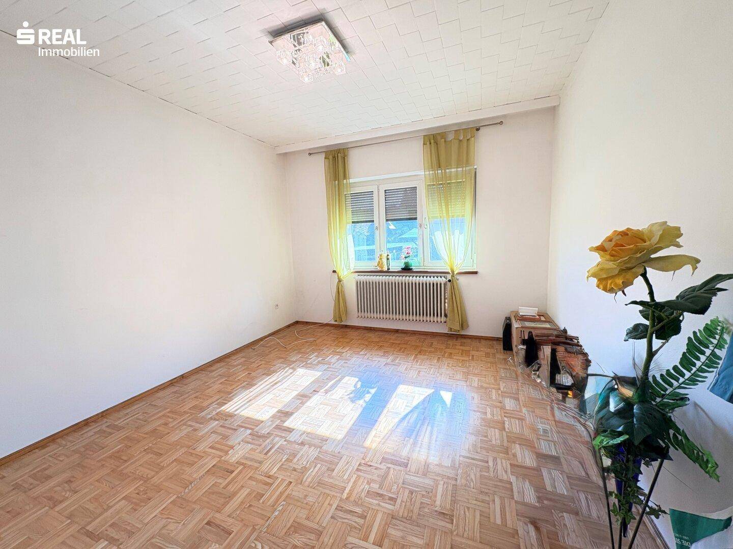 Helles Schlafzimmer mit Parkettboden und großem Fenster, das viel Tageslicht hereinlässt.