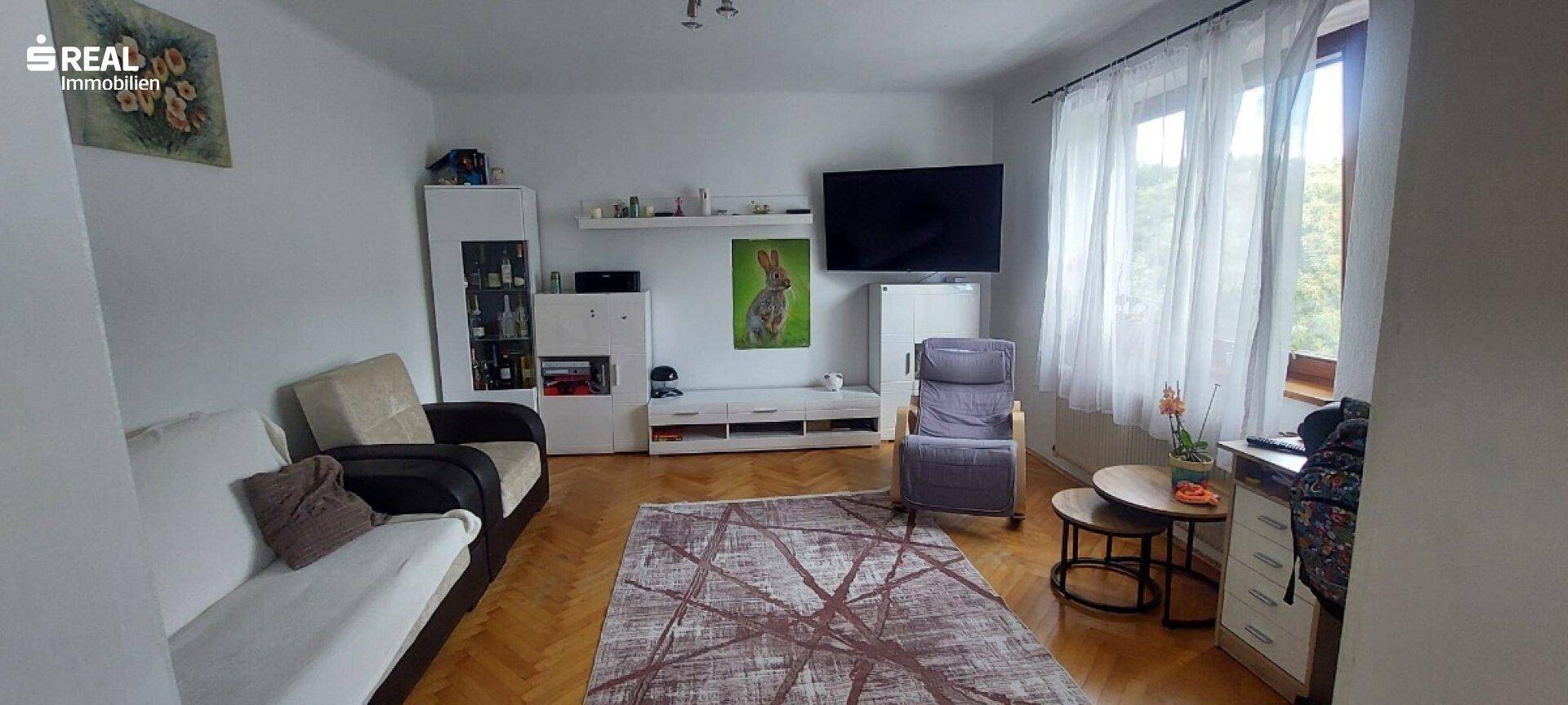 Helles Wohnzimmer mit Parkettboden, bequemen Sofas und einem Fernseher an der Wand.