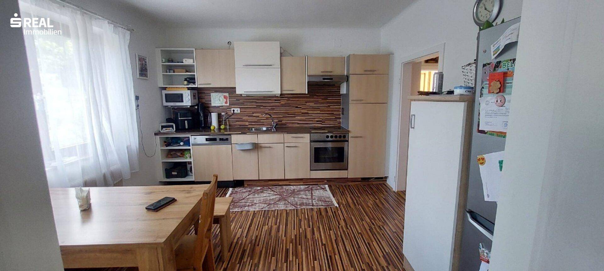 Funktionale Küche mit hellen Holzschränken, integrierten Geräten und Essbereich am Fenster.