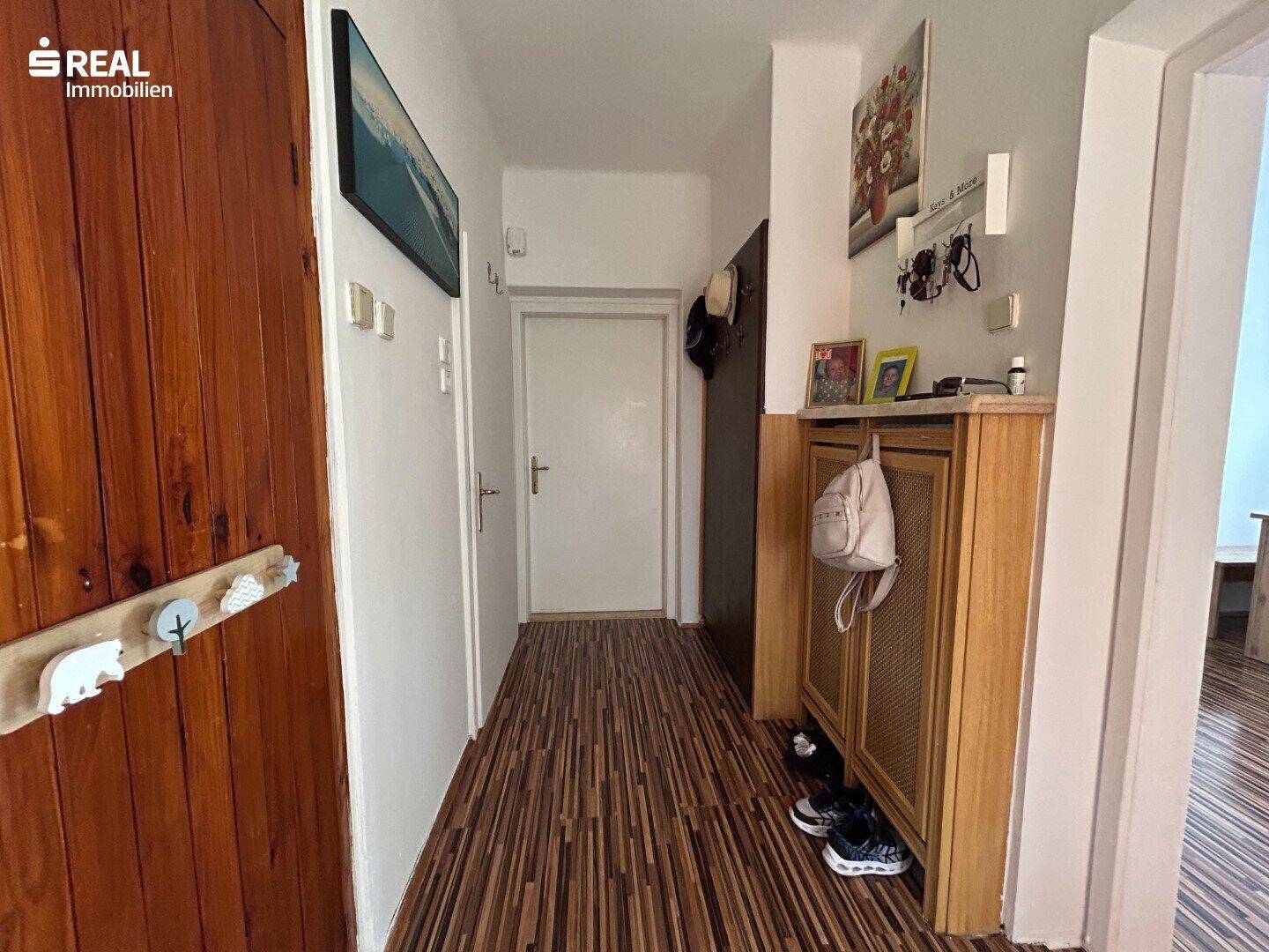 Langer Flur mit Holzfußboden, Garderobe und Zugang zu verschiedenen Räumen.