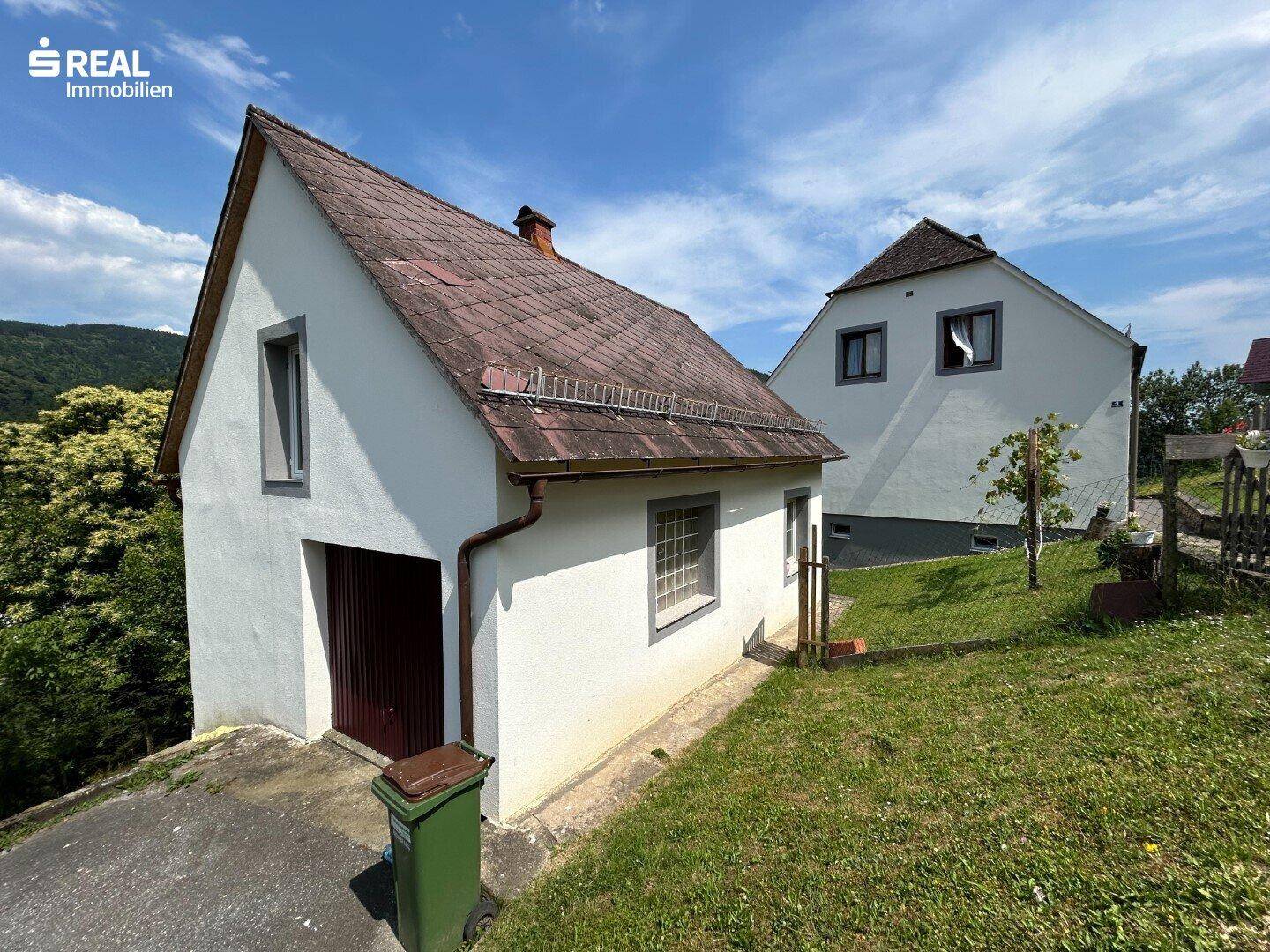 Nebengebäude mit Garage und weißer Fassade, umgeben von grüner Wiese.