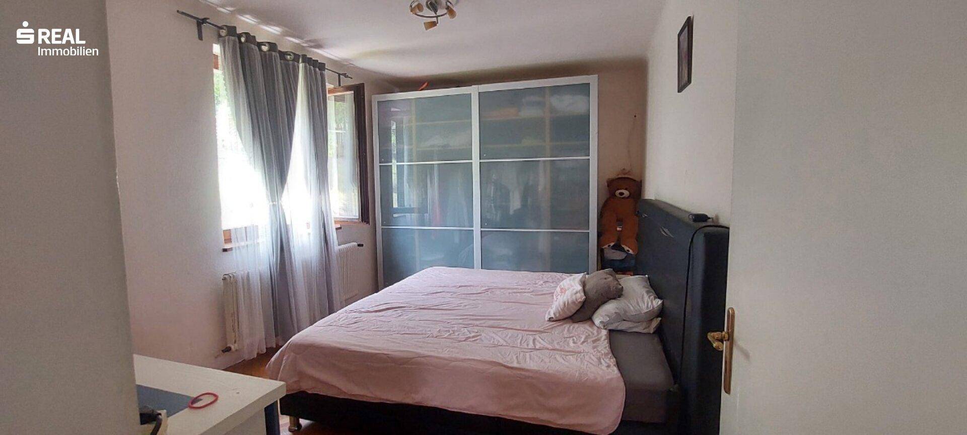 Schlafzimmer mit Doppelbett, großem Schiebeschrank und Fenster mit Vorhängen.