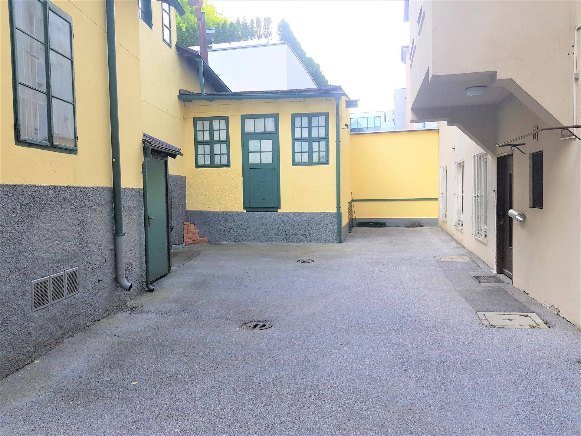 Hinterhofbereich mit gepflasterter Fläche und Nebengebäuden in gelber Farbe.