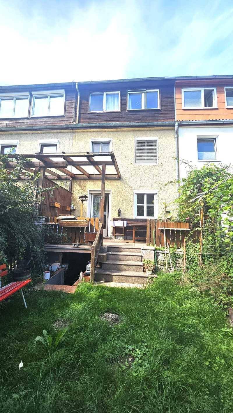 Hinterhof eines Reihenhauses mit Holzterrasse, Pergola und grünem Gartenbereich.