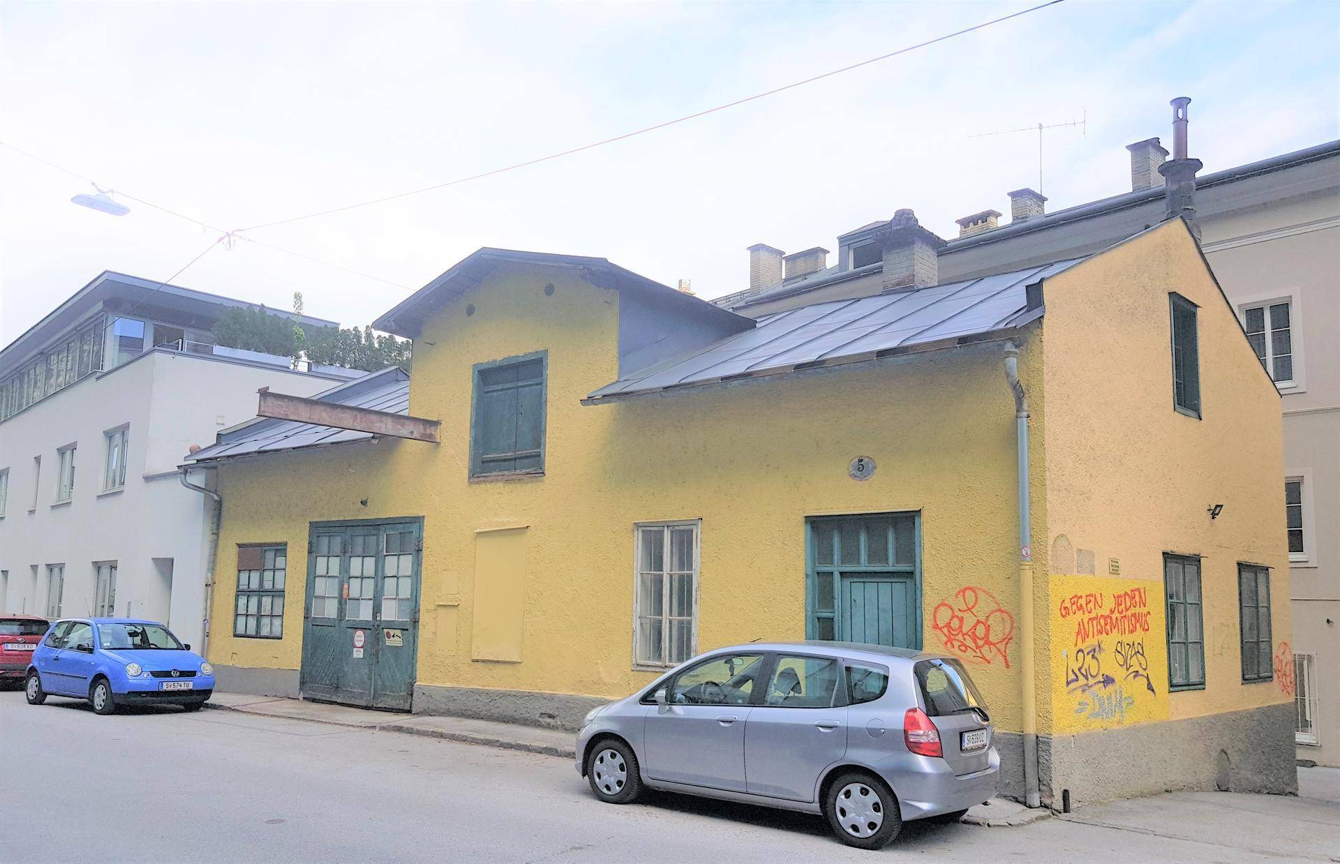 Gelbes Gebäude mit Satteldach und großen Holztoren an einer Straße mit parkenden Autos.