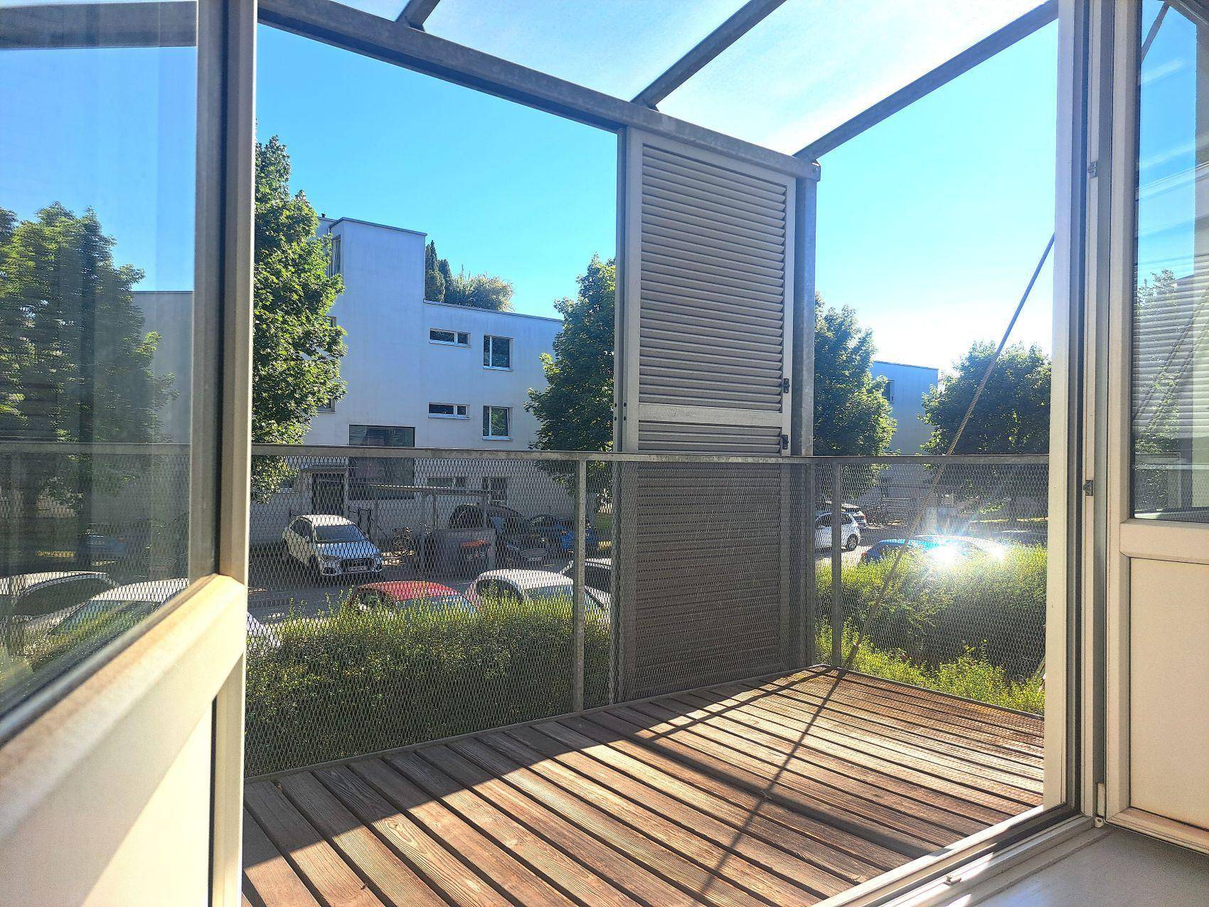 Sonnige Loggia mit Holzboden und Blick auf die modernen Wohngebäude und den Innenhof.