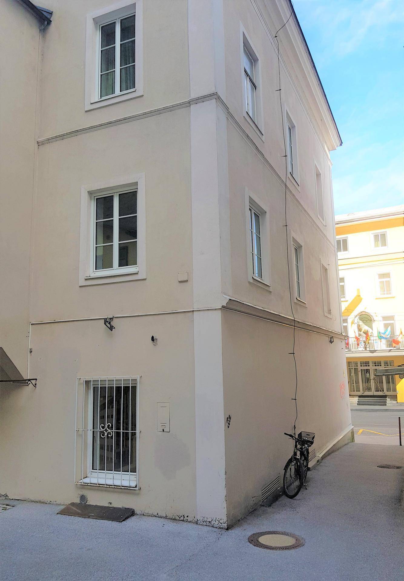 Seitenansicht des Gebäudes mit Fenstern und einem Fahrrad an der Wand in einer Gasse.