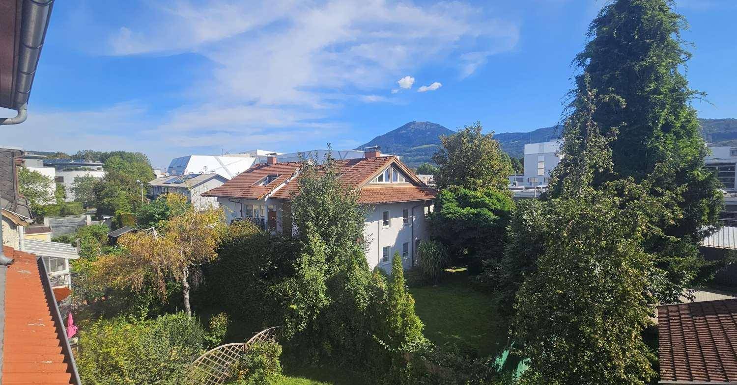 Haus mit Garten und Bäumen, umgeben von einer grünen Landschaft unter blauem Himmel.
