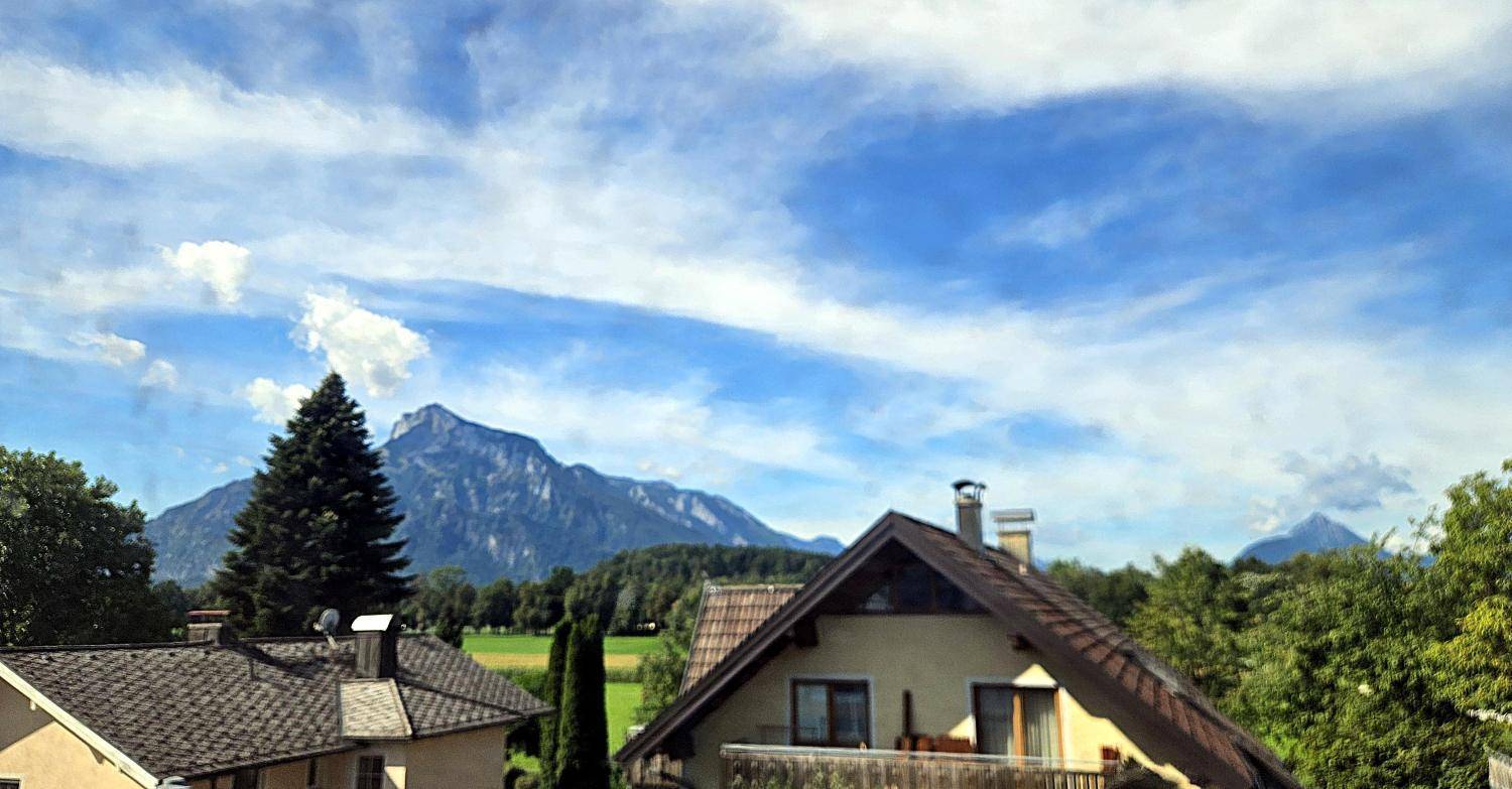 Panoramablick auf Wohnhäuser mit Balkonen und grüner Umgebung vor einer Bergkulisse.
