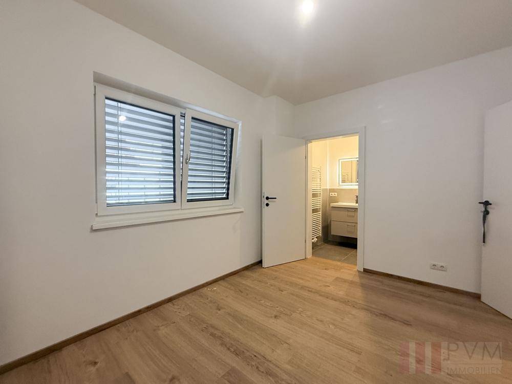 Helles Schlafzimmer mit Holzboden, Fenster und direktem Zugang zu einem eigenen Bad.